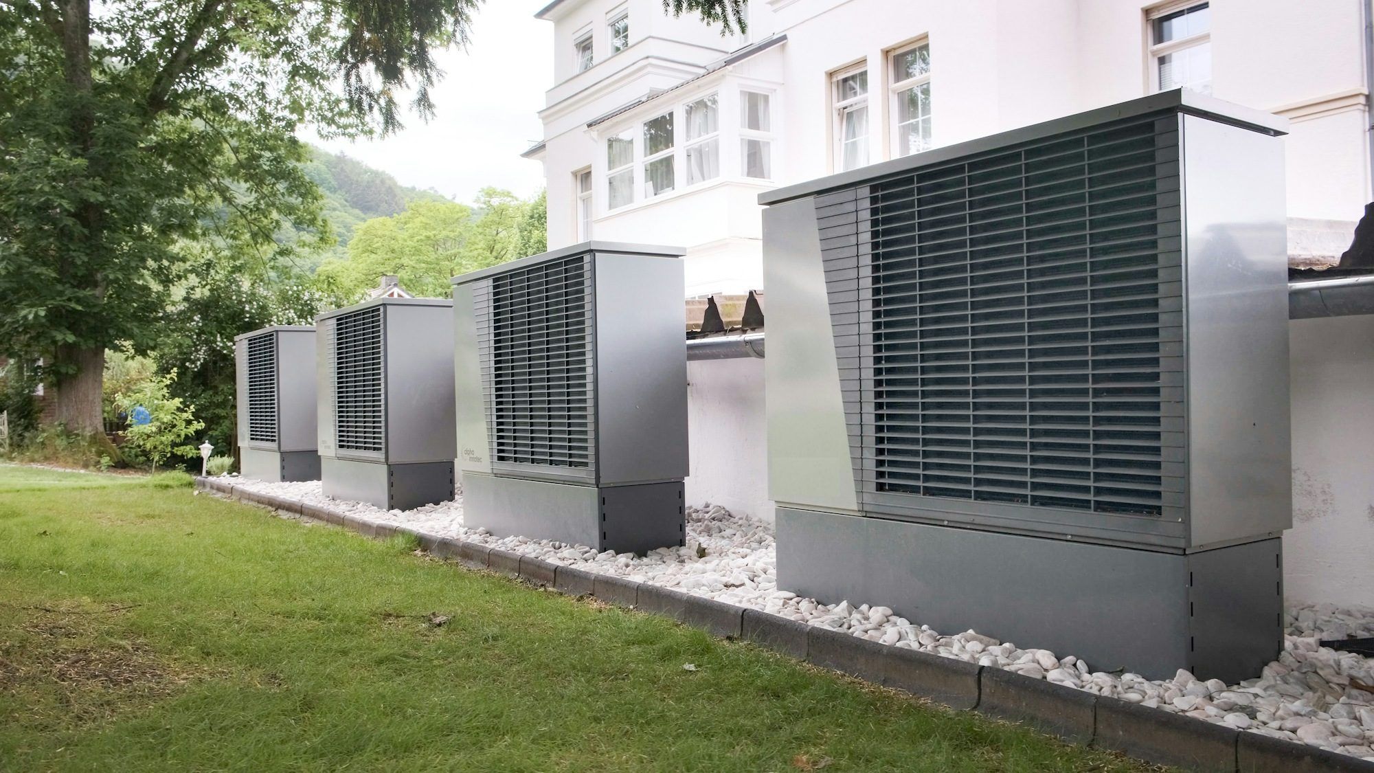 Quatre pompes à chaleur air-eau alignées devant un bâtiment, installées en cascade